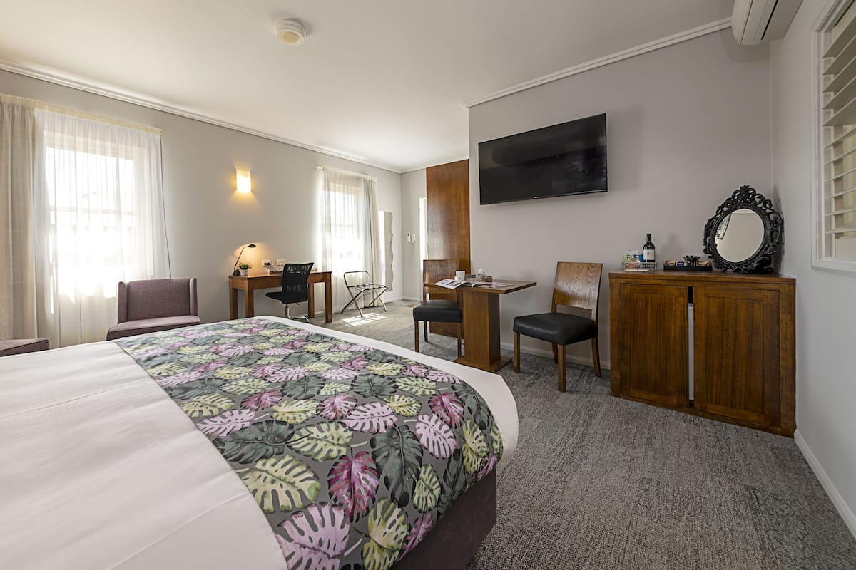 Una habitación de hotel con una cama, un escritorio, una silla, una televisión y un espejo.