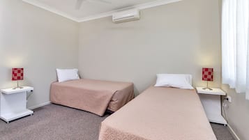 A hotel room with two single beds, a ceiling fan, an air conditioning unit, bedside lamps, and a carpeted floor.