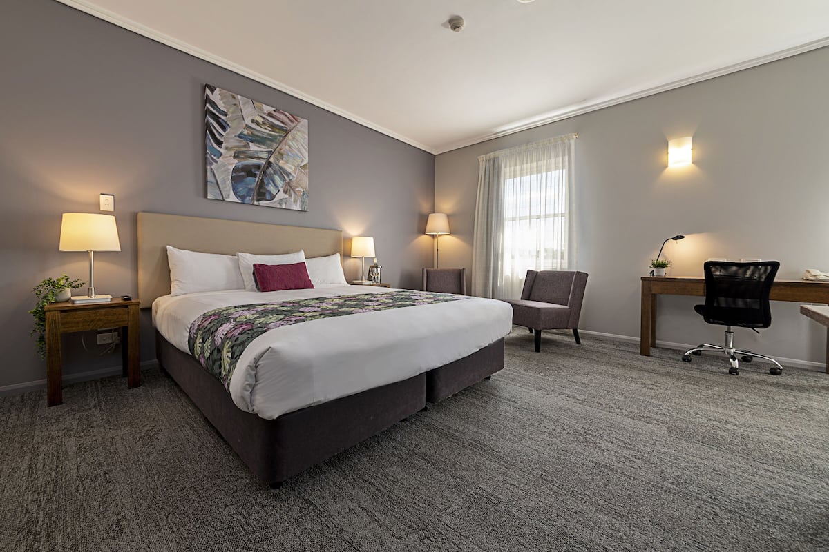 Habitación de hotel con una cama grande, dos mesitas de noche con lámparas, un escritorio con silla y una ventana con cortinas.