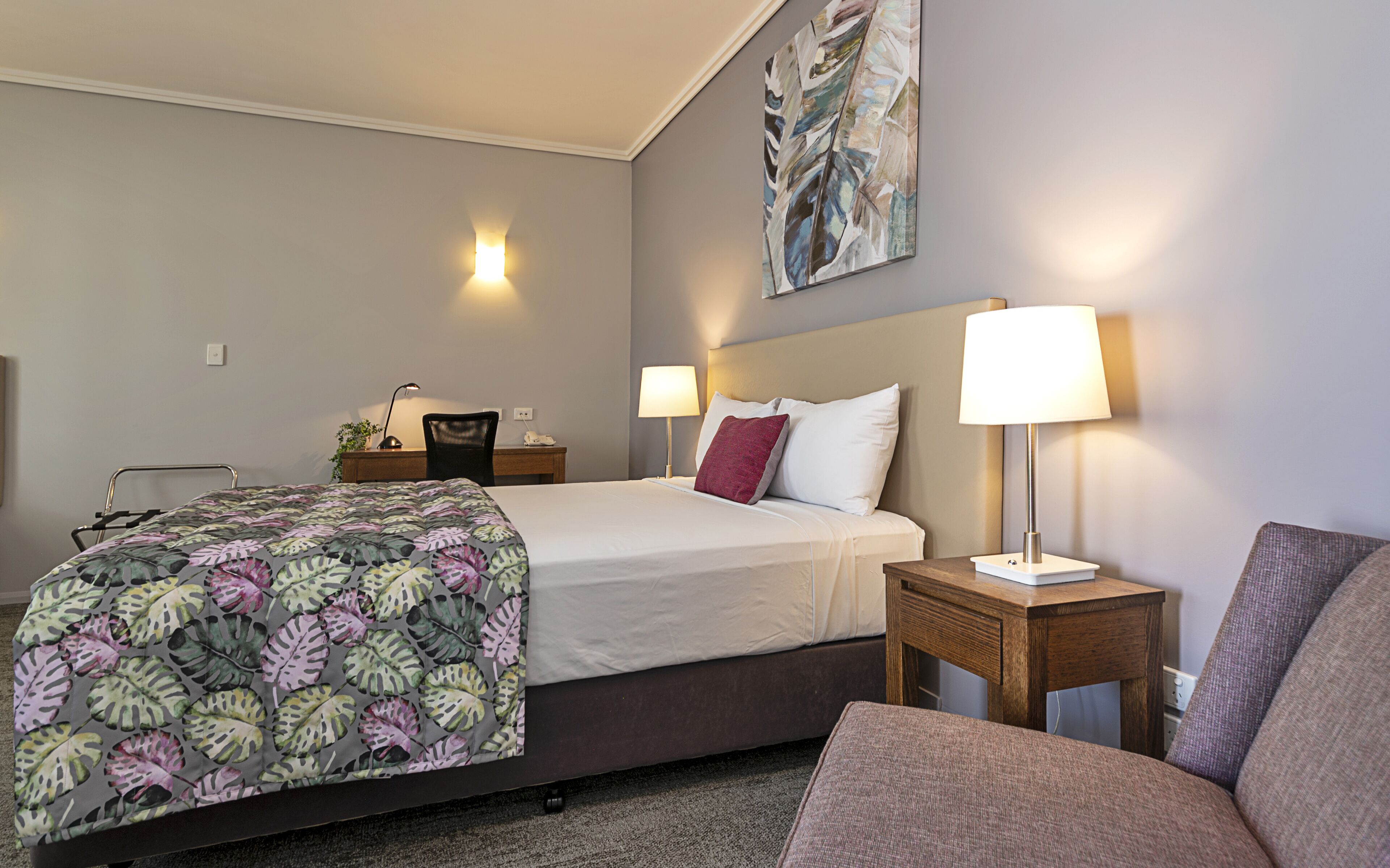 Une chambre d’hôtel avec un lit, des tables de chevet, un bureau, une chaise, une lampe et un tableau au mur.