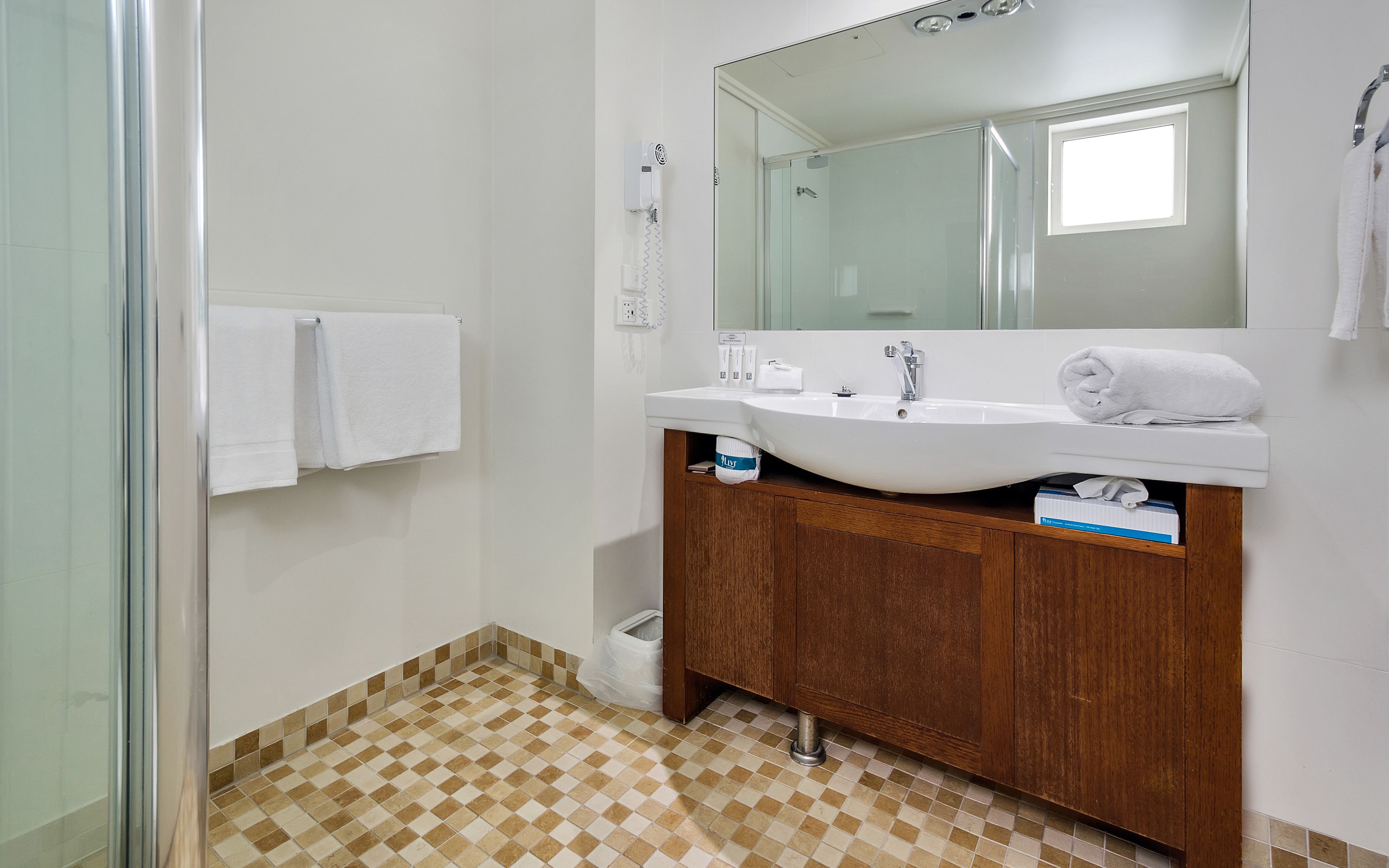 Een badkamer met een douchecabine van glas, een wit wastafelmeubel met een houten kast, en een spiegel boven de wastafel.