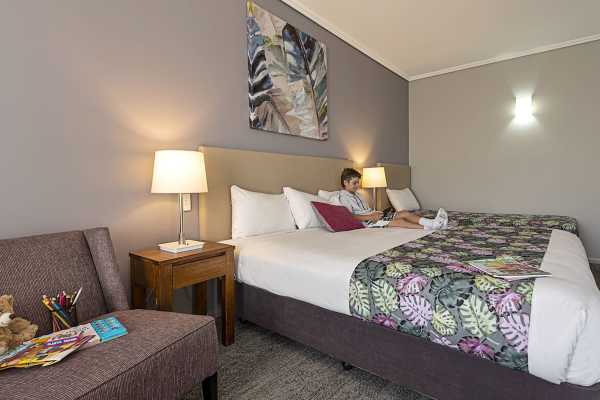 Una habitación de hotel con una cama, una mesita de noche, una silla y una obra de arte en la pared.