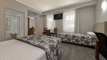 A hotel room with two beds, a desk, a chair, a TV, and a shower area.