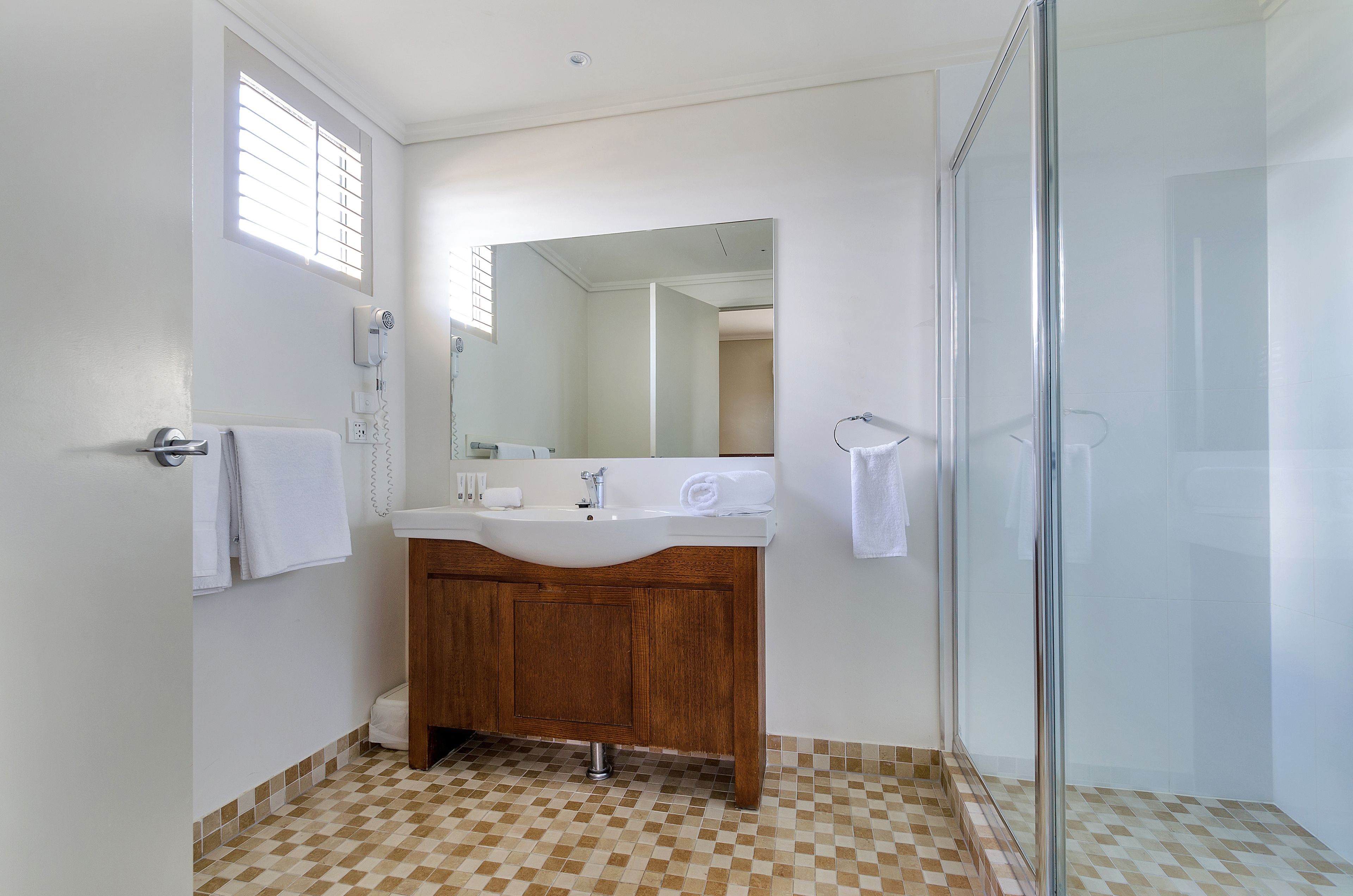 A bathroom with a wooden vanity, a white sink, a mirror, and a glass shower enclosure.