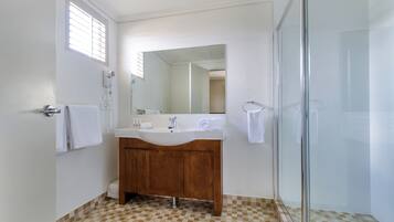 A bathroom with a wooden vanity, a white sink, a mirror, and a glass shower enclosure.