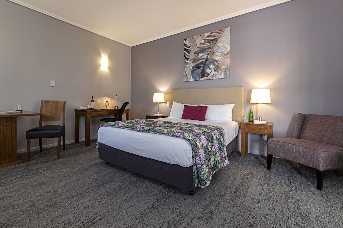 Habitación de hotel con cama, escritorio, silla y dos lámparas de noche.