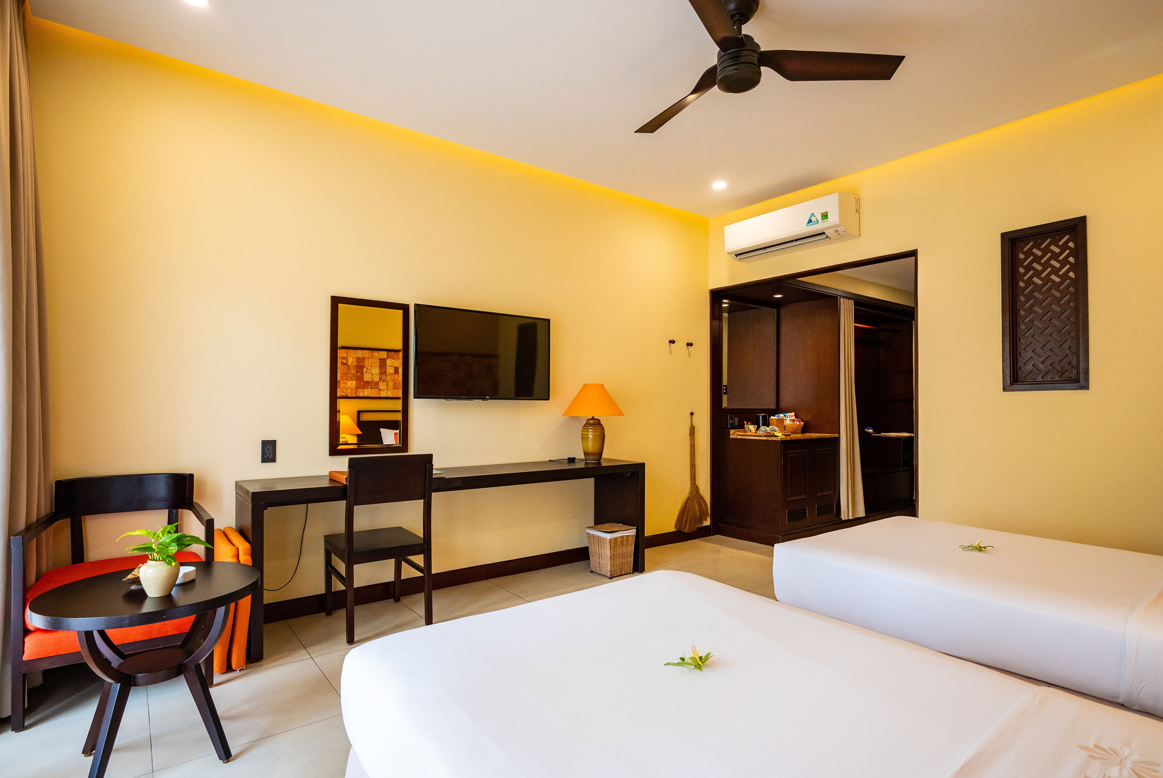 Habitación de hotel con cama, escritorio, silla, lámpara, ventilador de techo y aire acondicionado.