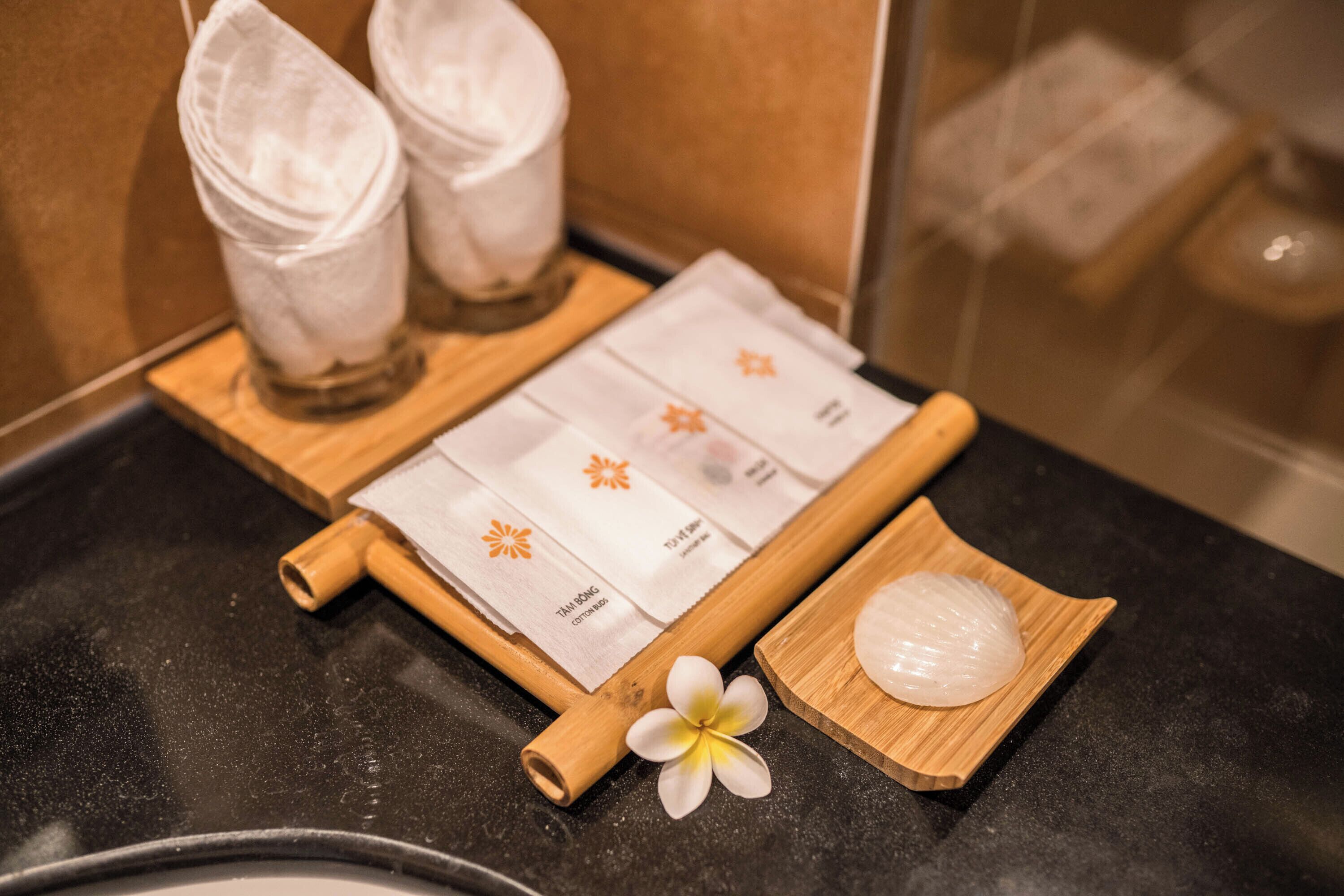 A bathroom with a black countertop, a wooden tray with a white flower, a rolled-up towel, and two white towels hanging on a rack.