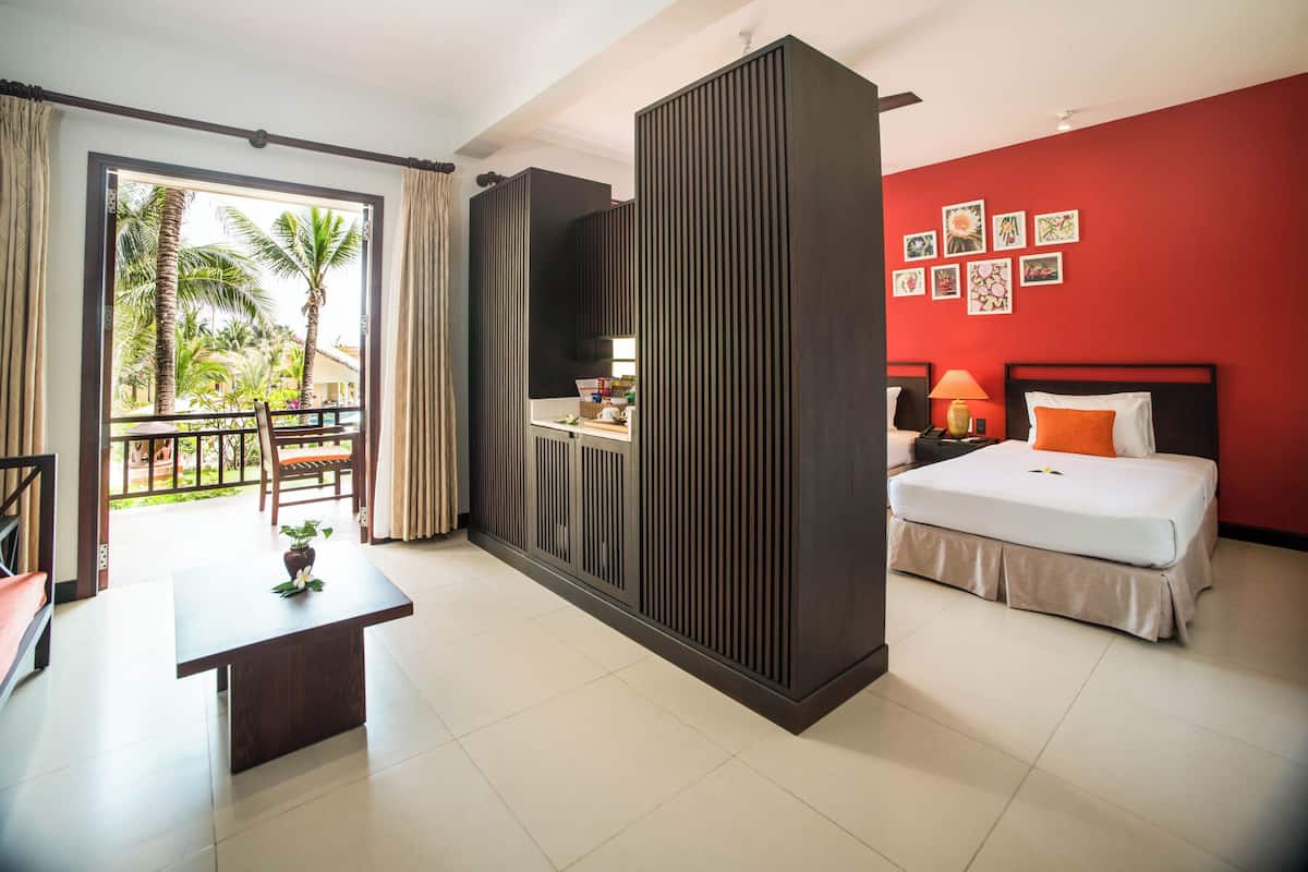 Une chambre d’hôtel avec un lit, un bureau, une vue sur les palmiers et un balcon.