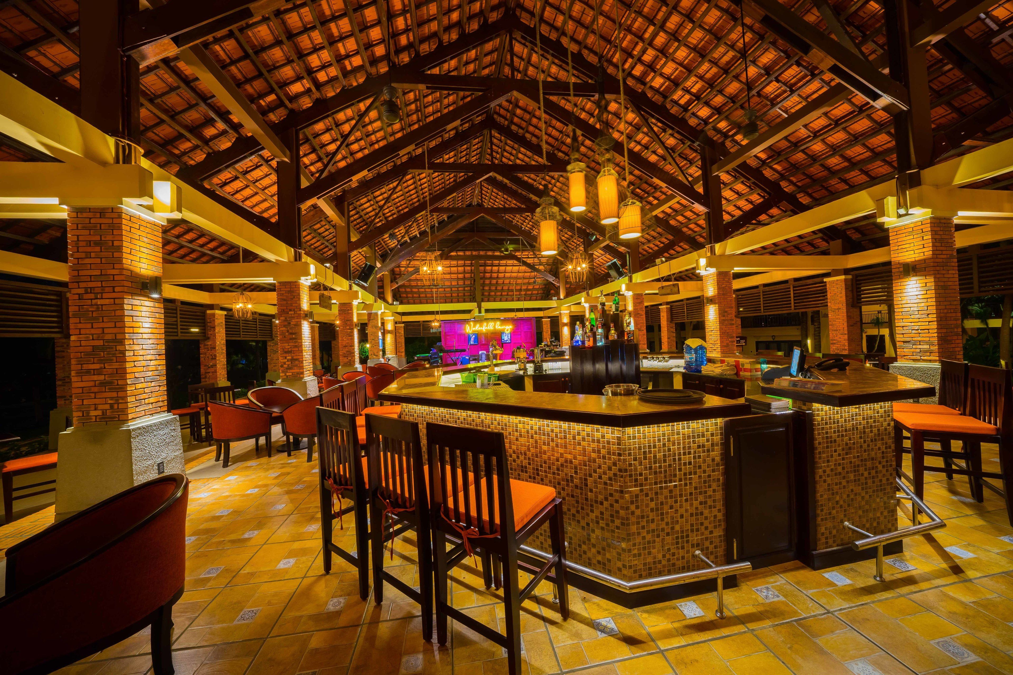 A spacious bar area with a high ceiling and brick accents, featuring multiple seating arrangements and a central bar counter.