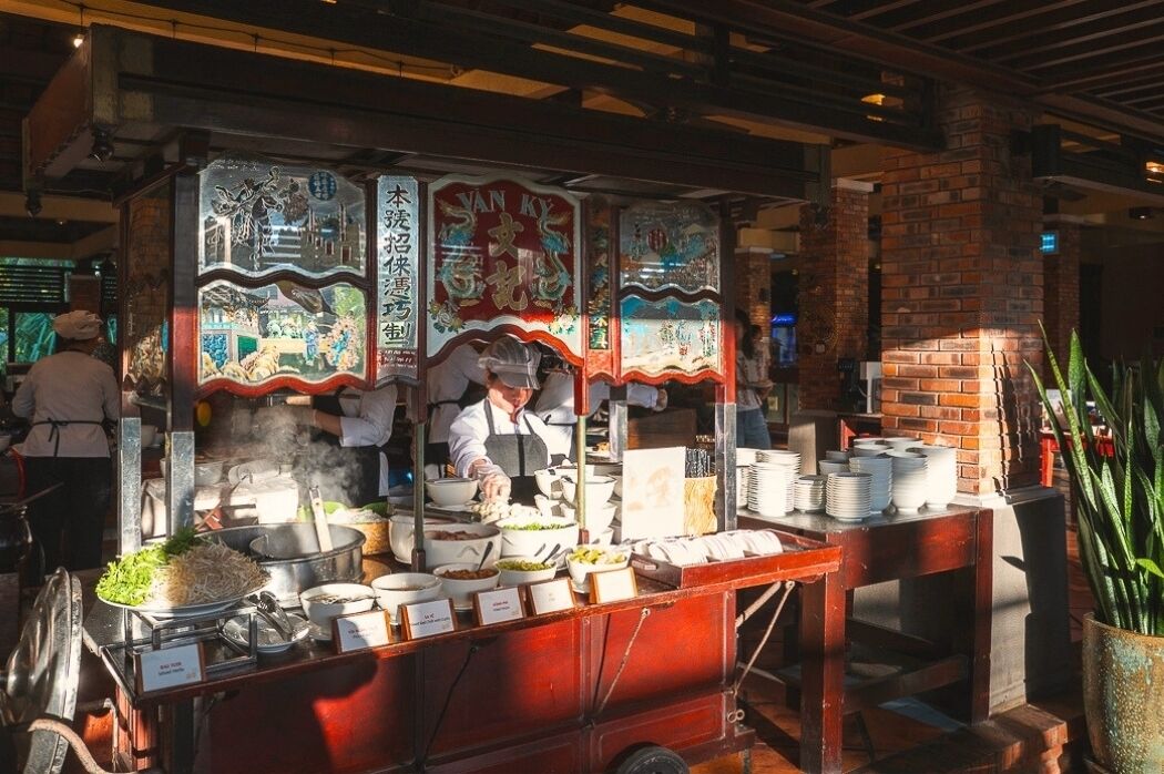 Ein Essensstand mit traditioneller chinesischer Dekoration, ein Koch der zubereitet und eine Backsteinwand im Hintergrund.