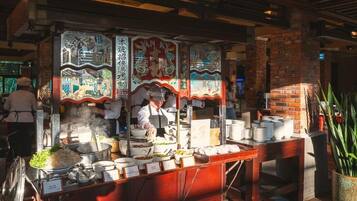 Een kraam met traditionele Chinese decoraties, een kok die eten bereidt, en een bakstenen muur op de achtergrond.