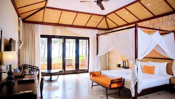 A room with a four-poster bed, a desk with a lamp, and a view through a glass door.