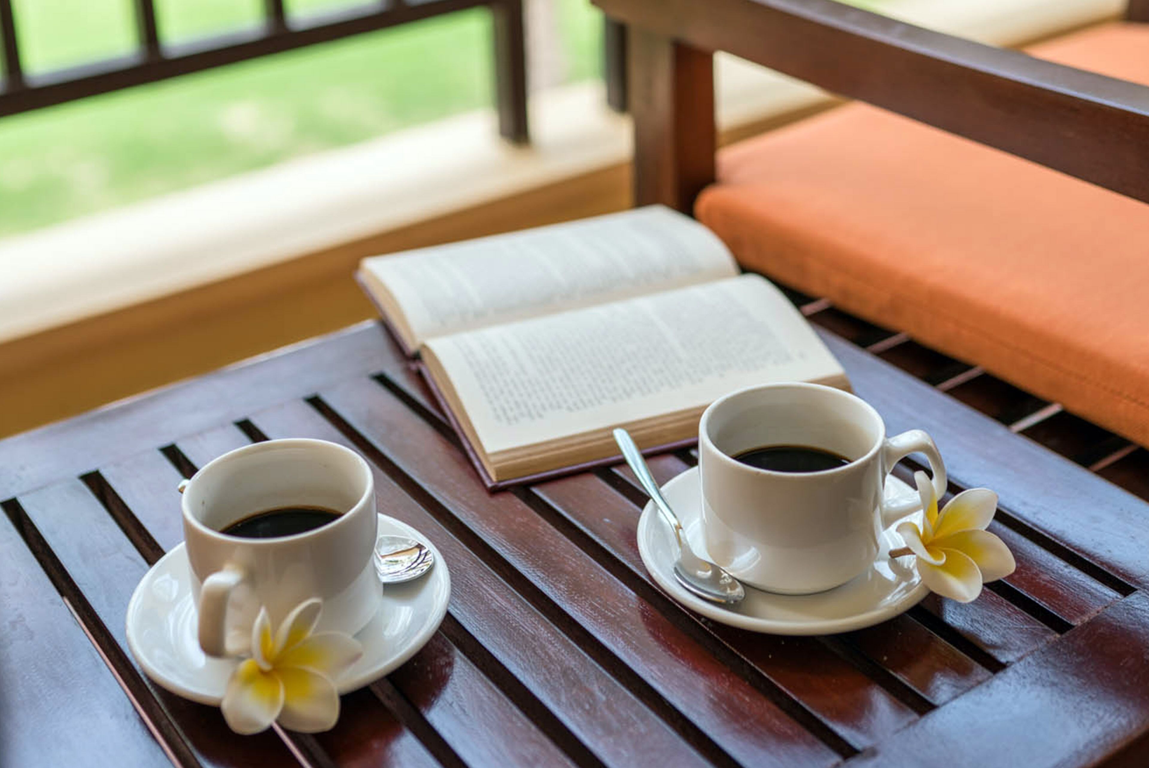 Una mesa de madera con dos tazas blancas de café, un libro y una flor.