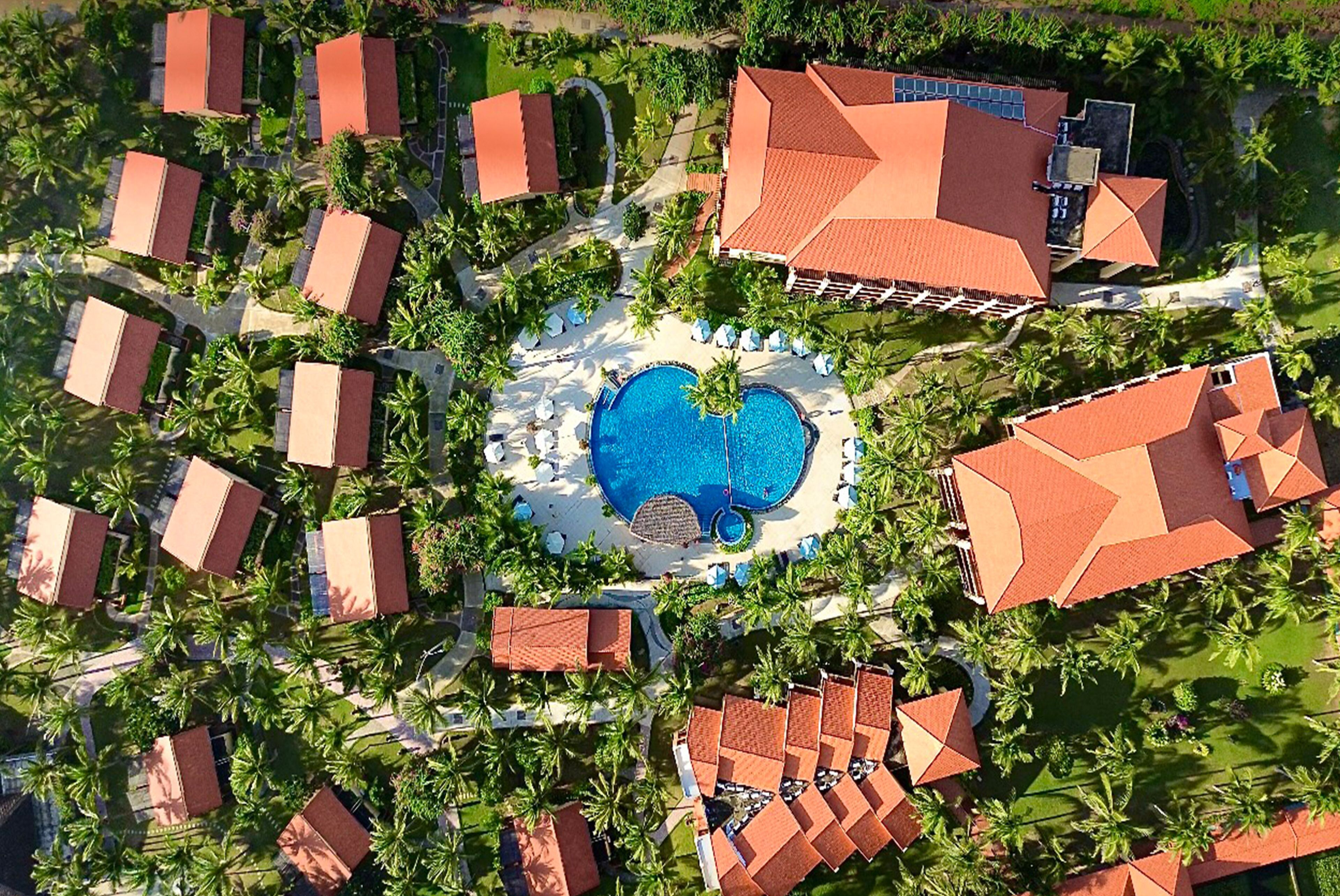 Luchtbeeld van een resort met een centraal zwembad, meerdere bungalows en palmbomen.