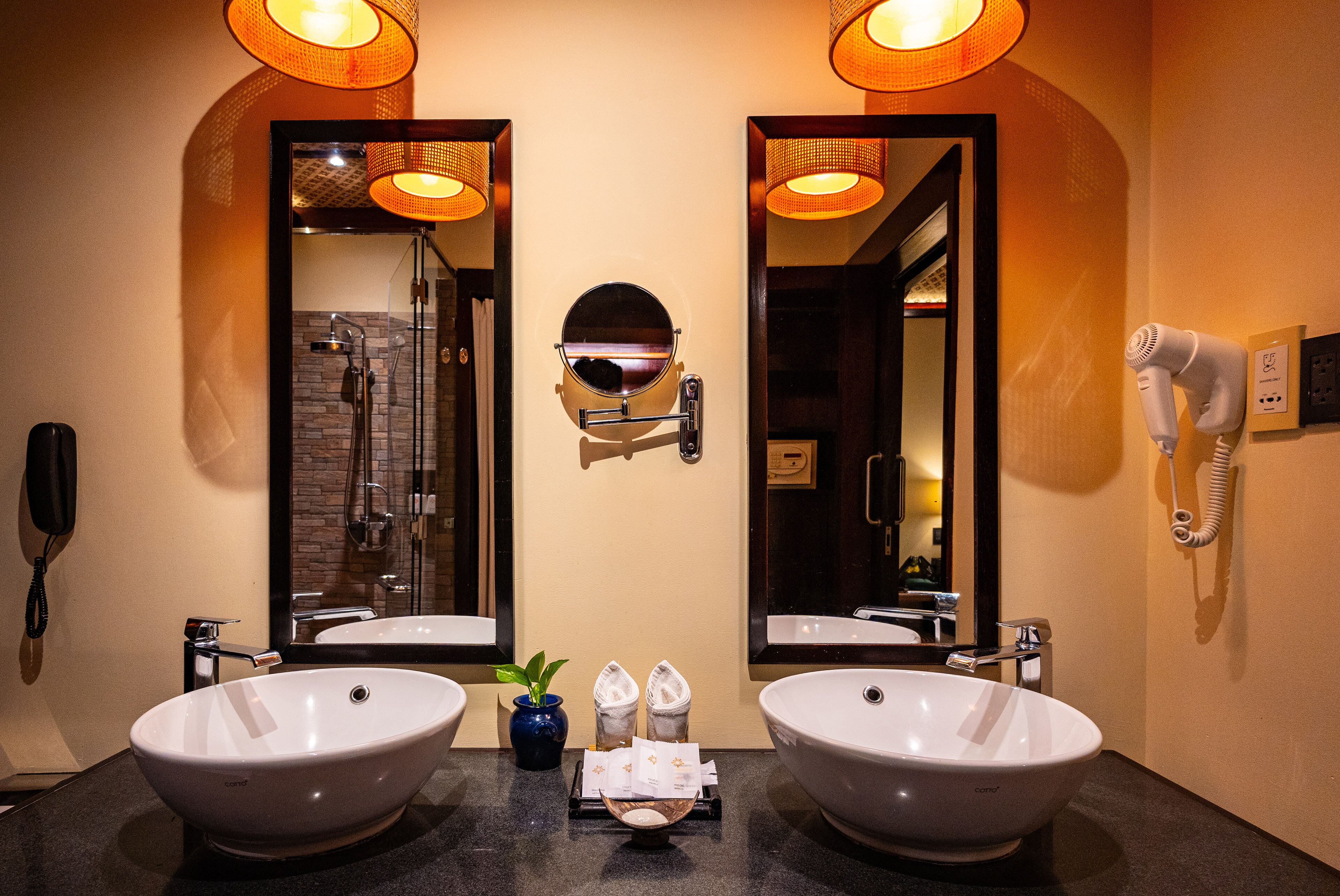 A bathroom with two large sinks, a mirror, a hairdryer, and a phone on the wall.