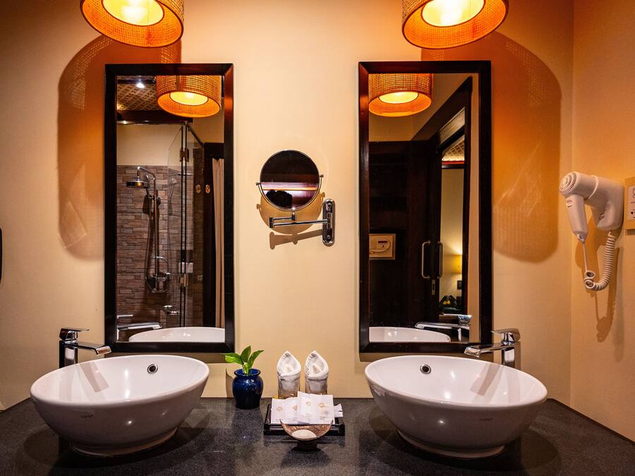 A bathroom with two large sinks, a mirror, a hairdryer, and a phone on the wall.