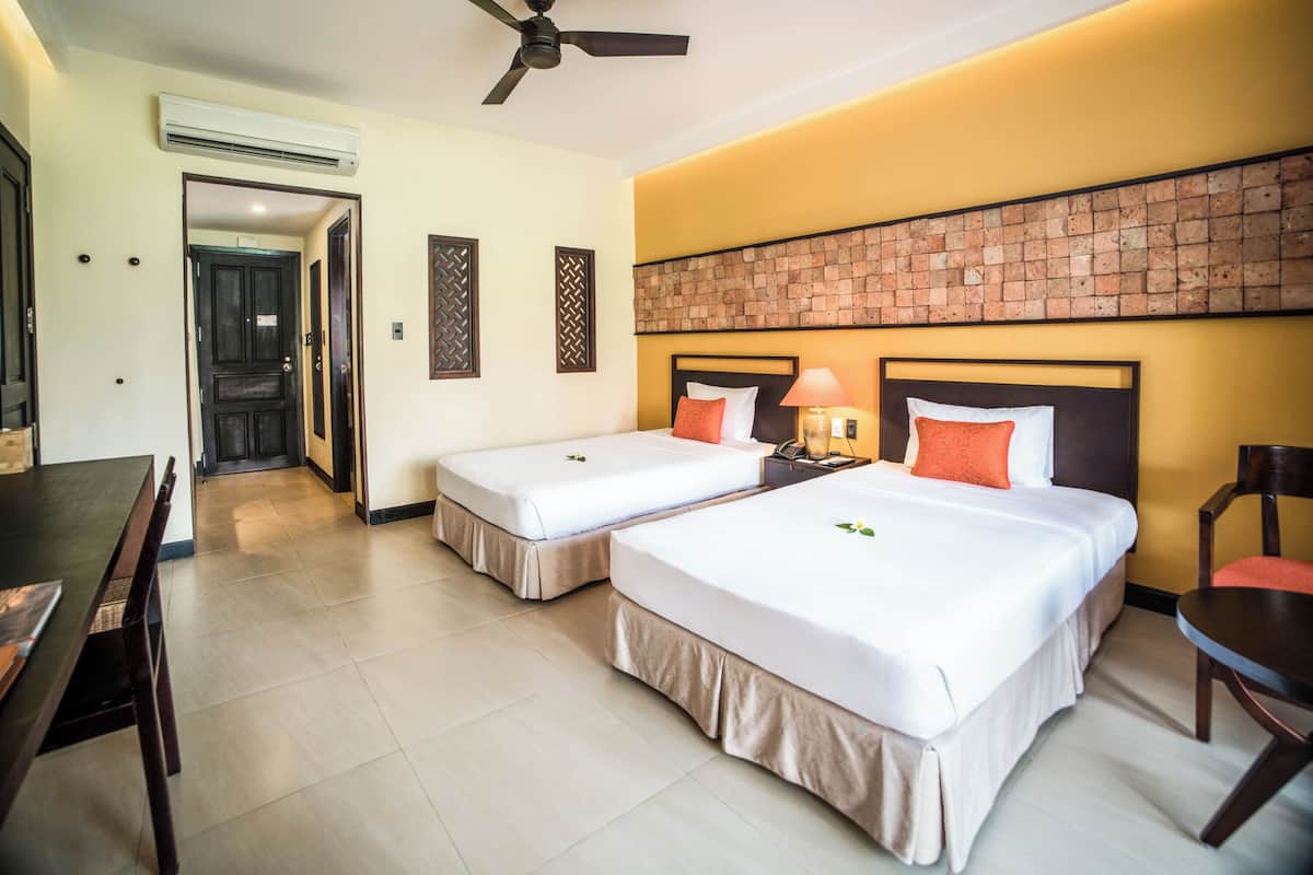 Une chambre d’hôtel avec deux lits, une table à manger, une chaise et un ventilateur de plafond.