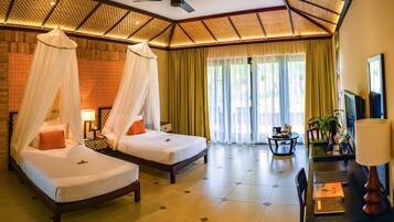 A hotel room with two beds, a desk, a chair, a TV, and a ceiling fan.