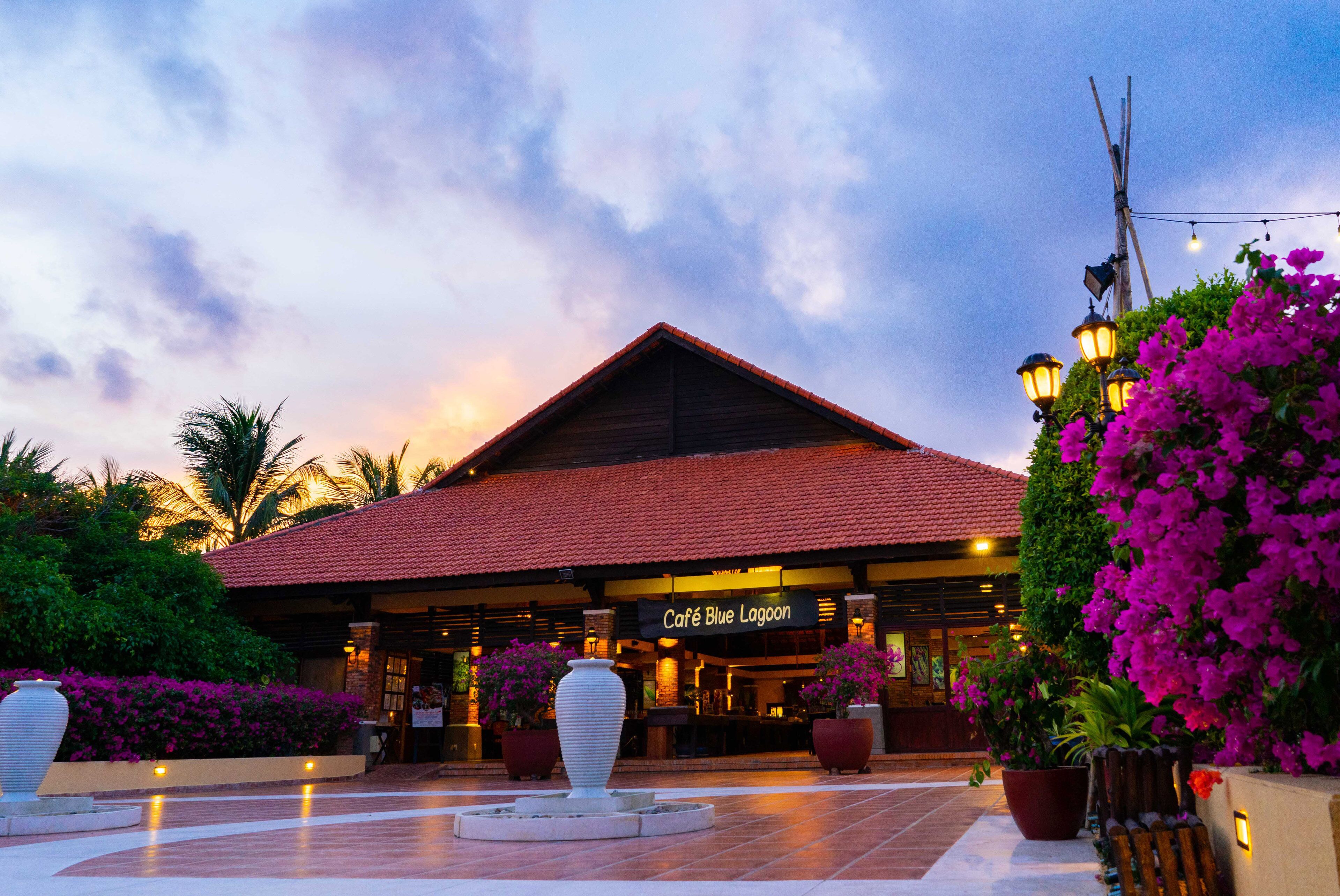 A building with a sign reading 'Café Blue Lagoon,' surrounded by potted plants and a tiled courtyard.