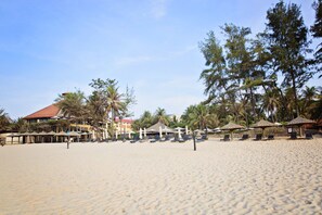 Di pantai, pasir putih, kursi berjemur, dan payung pantai