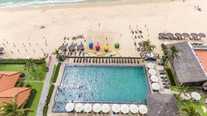 Vista aérea de un complejo turístico con piscina, tumbonas, sombrillas y zona de playa.