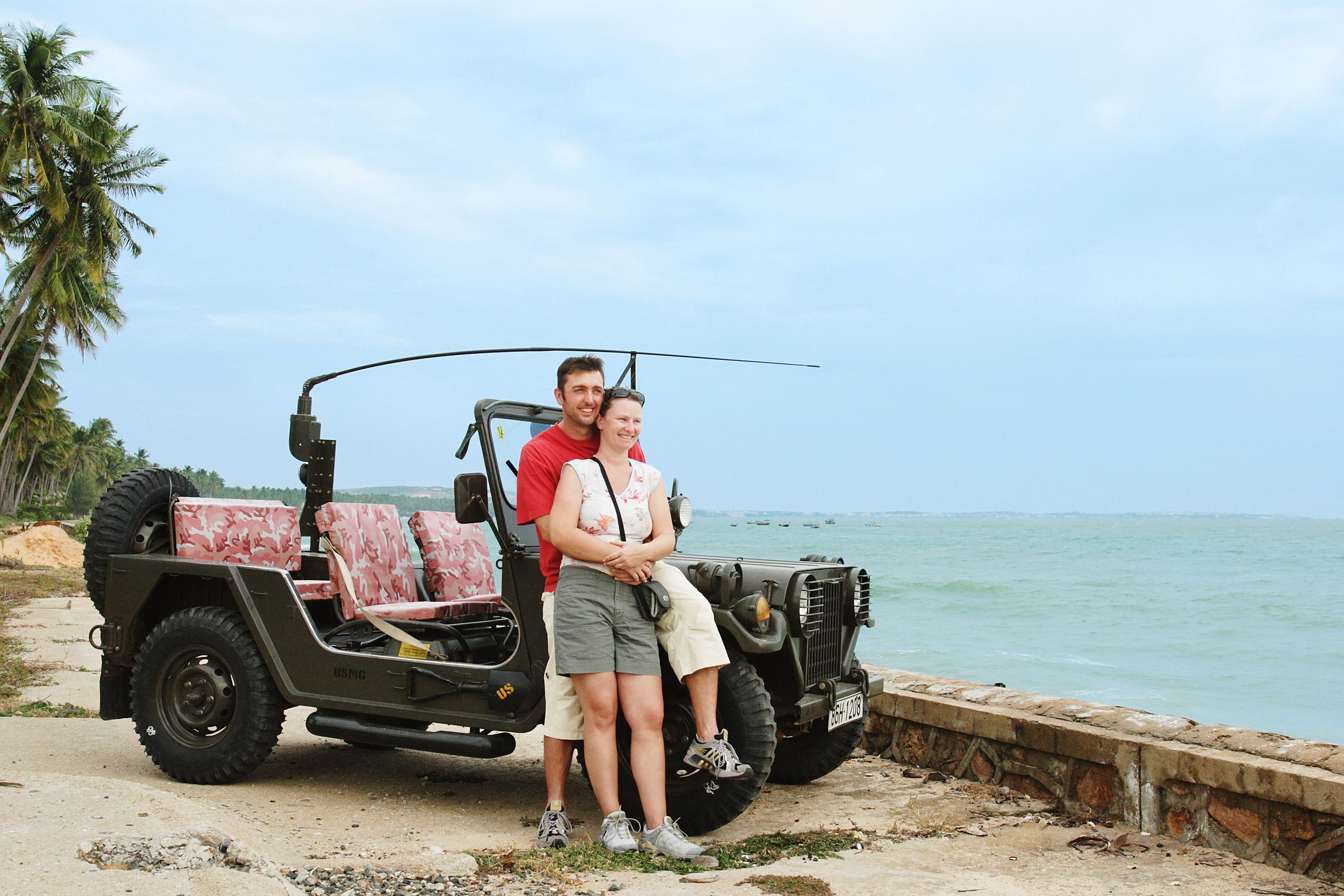 Un jeep estacionado junto a la playa con dos personas a su lado.
