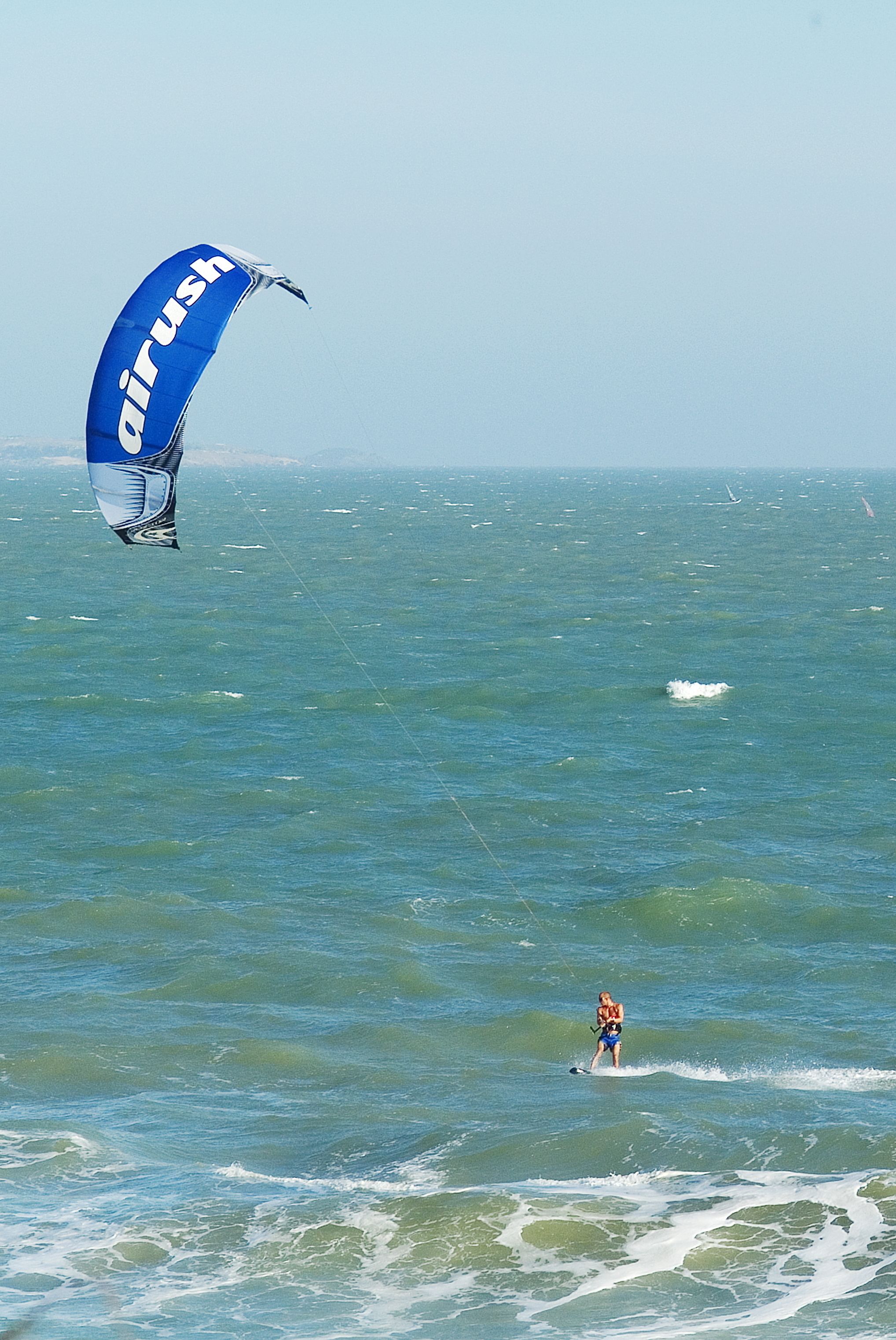 Uma pessoa praticando windsurf com uma vela azul e branca.
