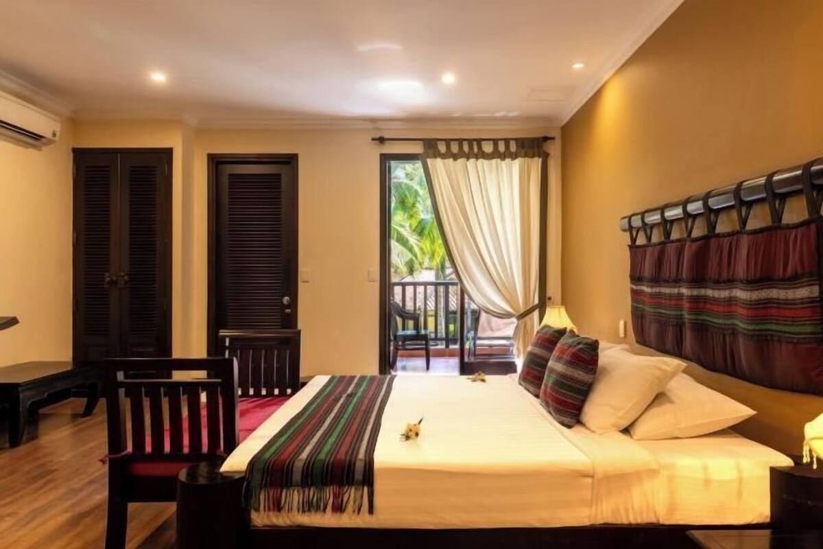 A hotel room with a bed, a chair, a desk, and a balcony with curtains.