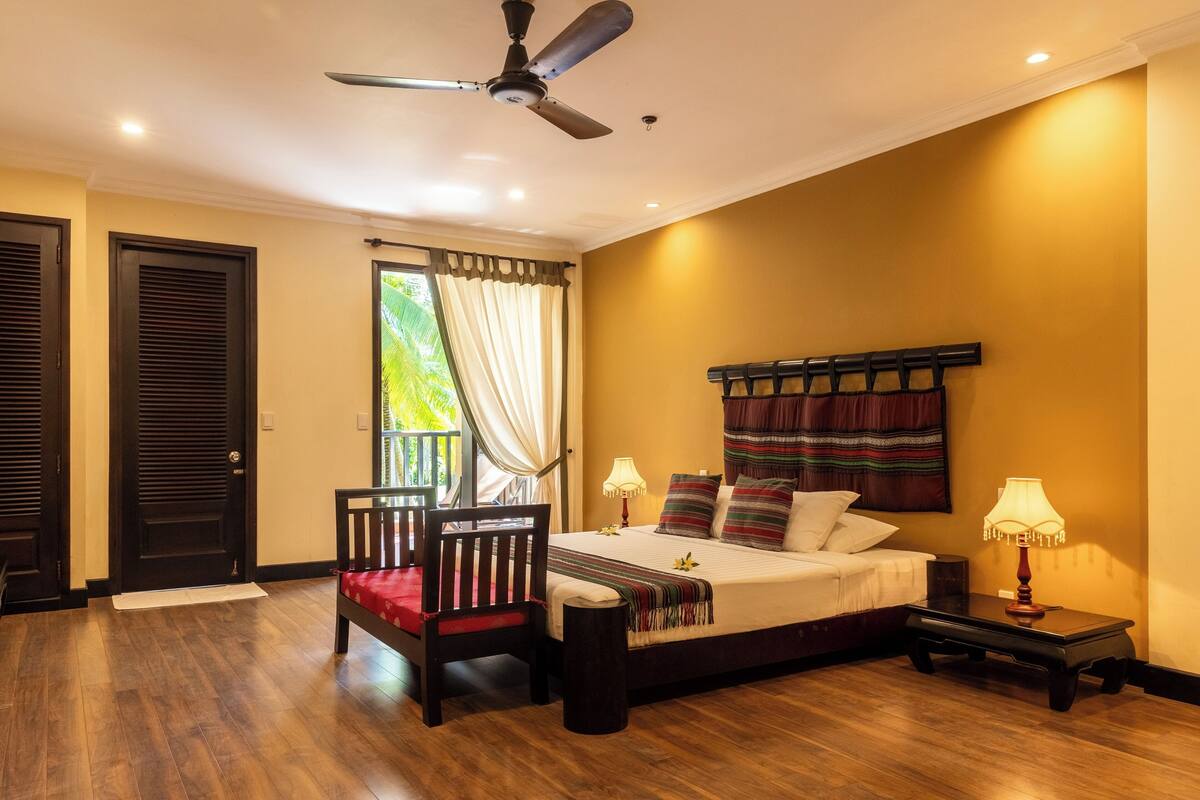 A bedroom with a bed, bedside tables, a chair, a ceiling fan, and a window with curtains.