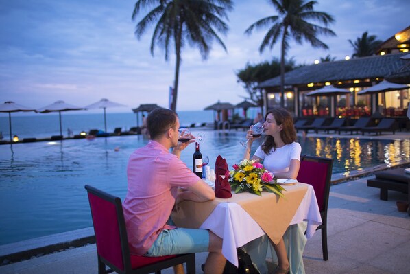 A couple dining by a poolside with a view of the ocean and palm trees. - Seahorse Resort & Spa (Mui Ne)