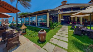 Un resort con asientos al aire libre, una edificación con techo de paja y vista a la playa.
