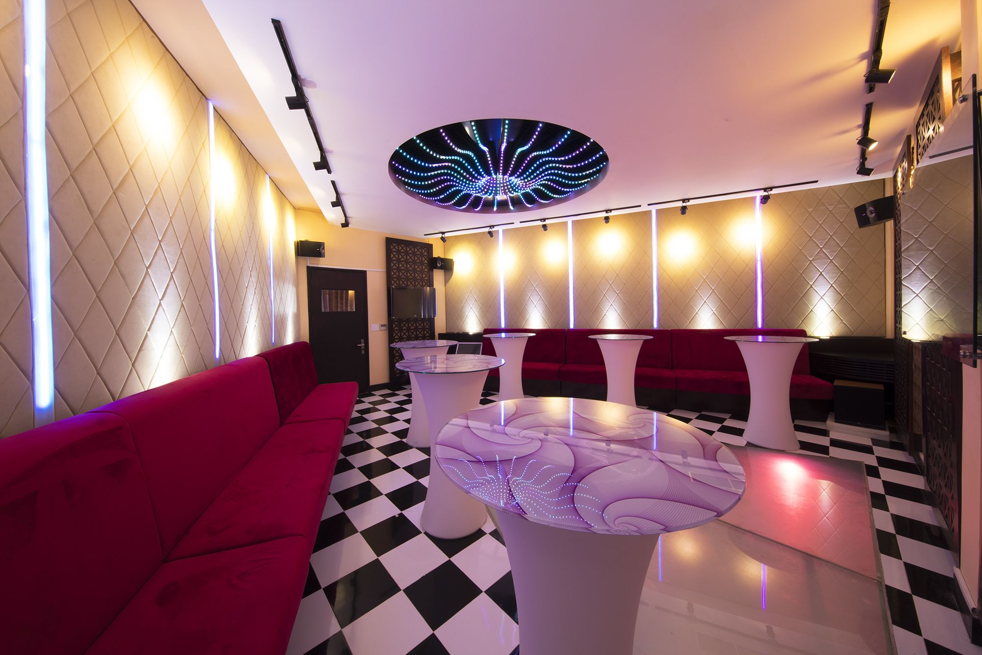 A modern lounge area with a checkered floor, red seating, and unique ceiling lighting.