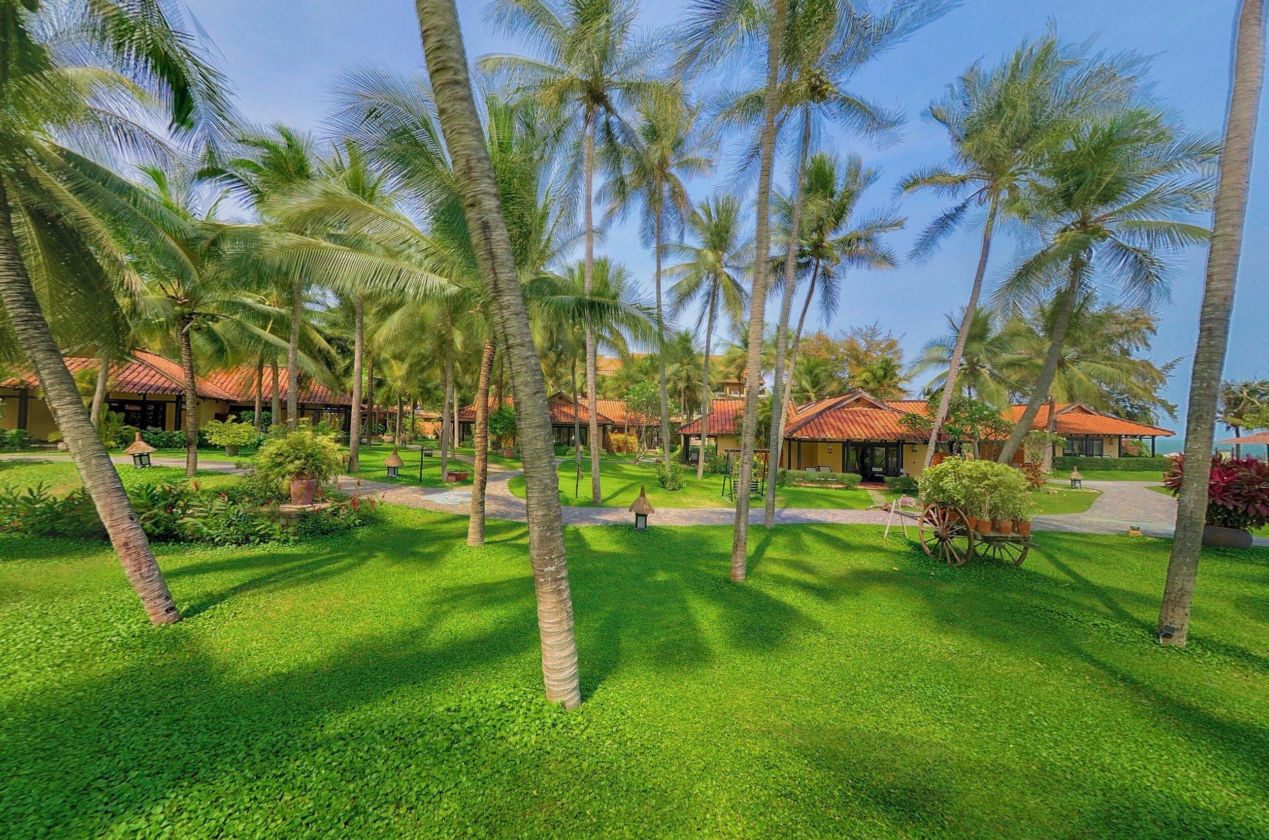 A tropical resort with palm trees, well-maintained lawns, and traditional-style buildings with red roofs.