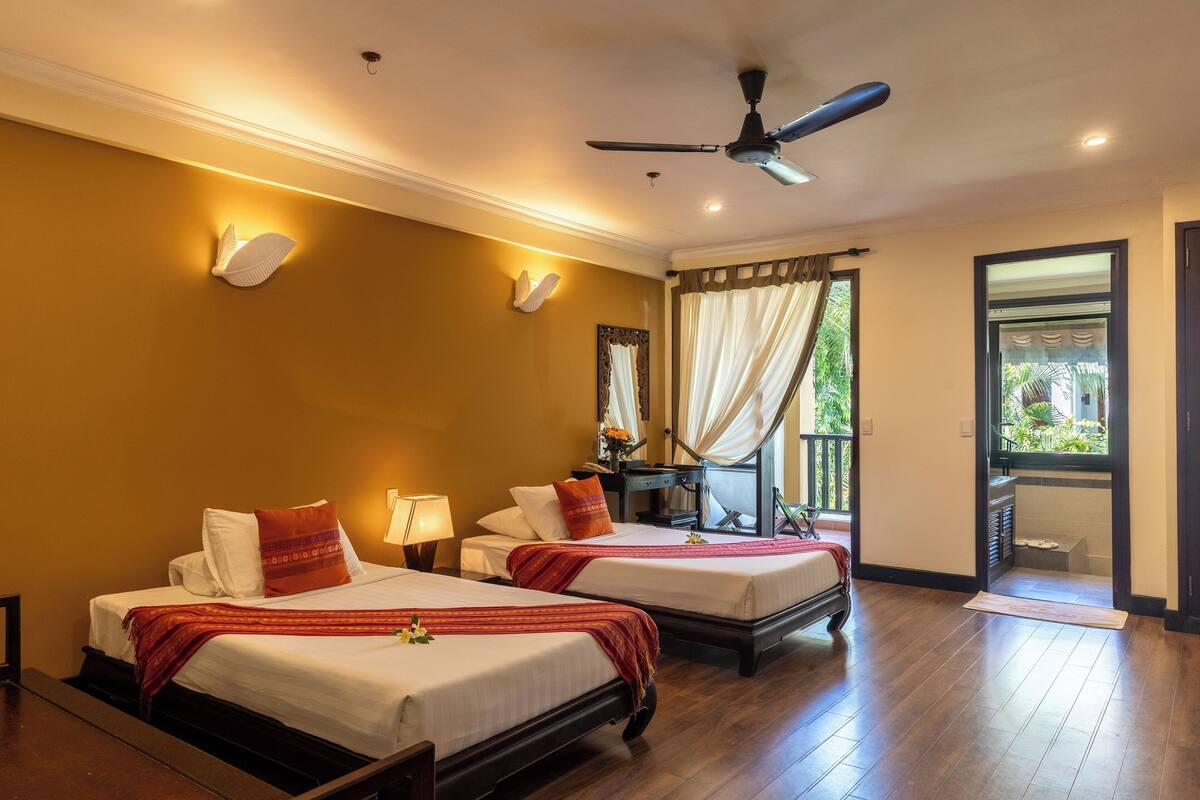 A hotel room with two beds, a ceiling fan, and a view of the outdoors.
