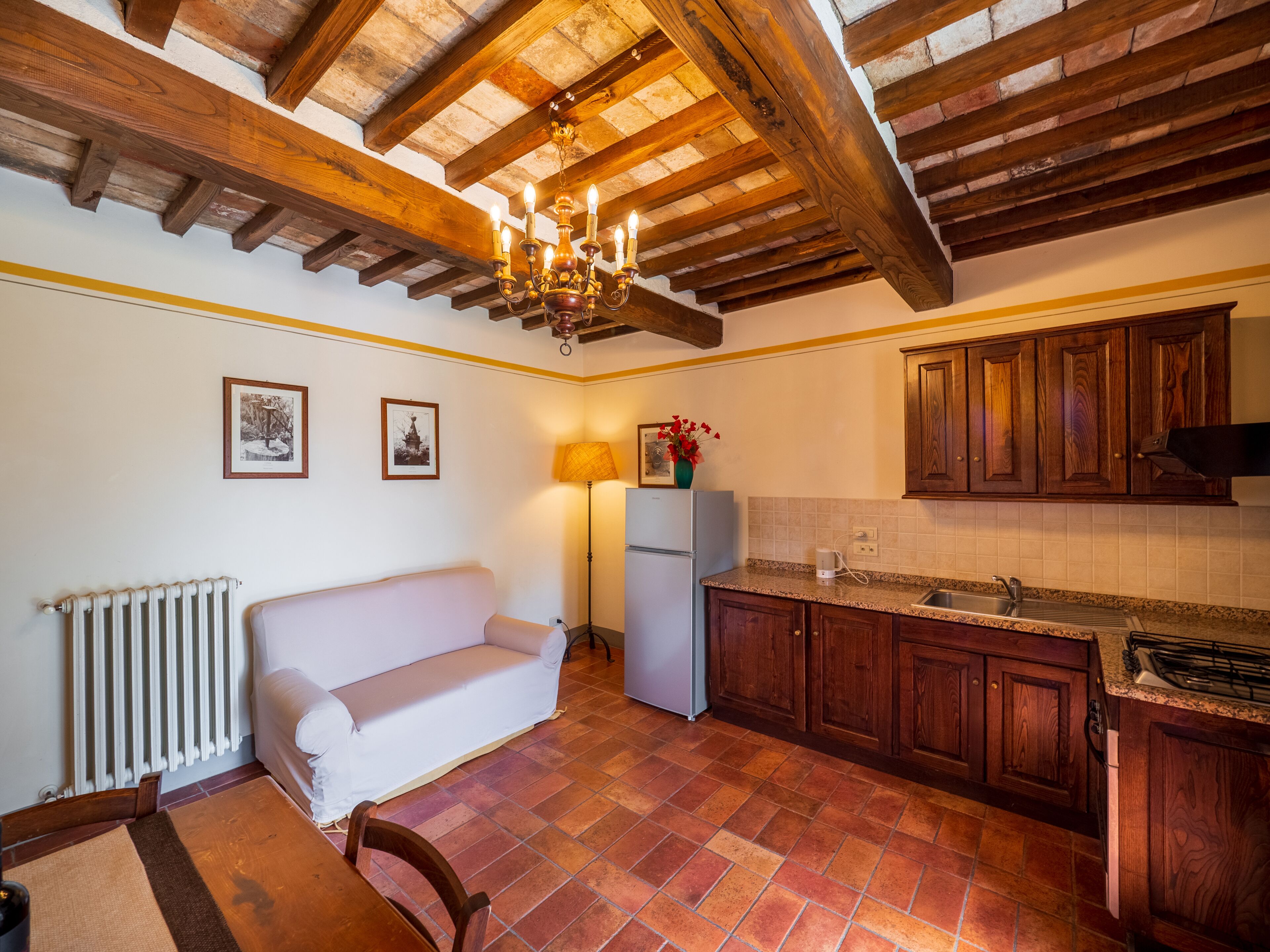 A cozy kitchen with wooden beams, a white sofa, and a tiled floor.
