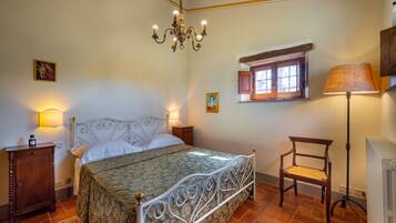 Ein Schlafzimmer mit Bett, Nachttisch, Sessel, Lampe, Fenster und einer Chandelier.
