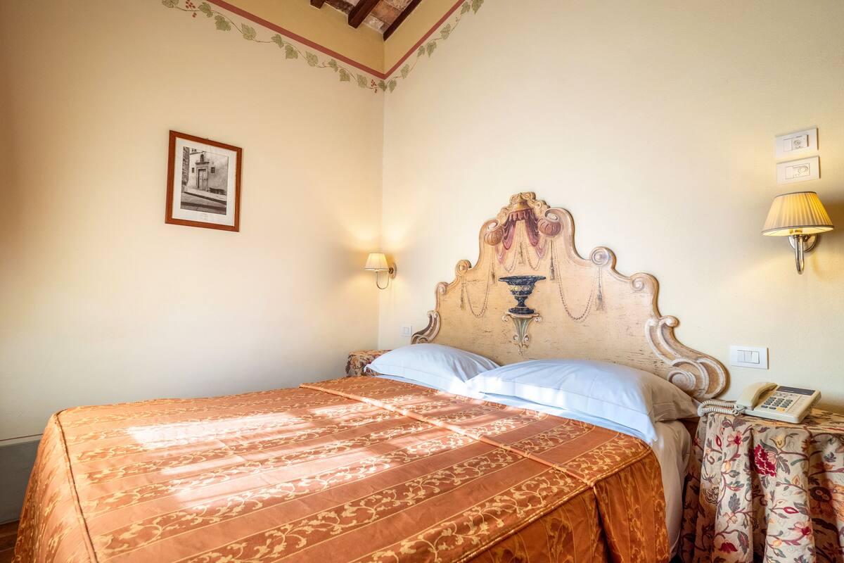 Un lit avec une couvre-lit à motifs, une tête de lit décorative, une lampe fixée au mur et un tableau encadré accroché au mur.