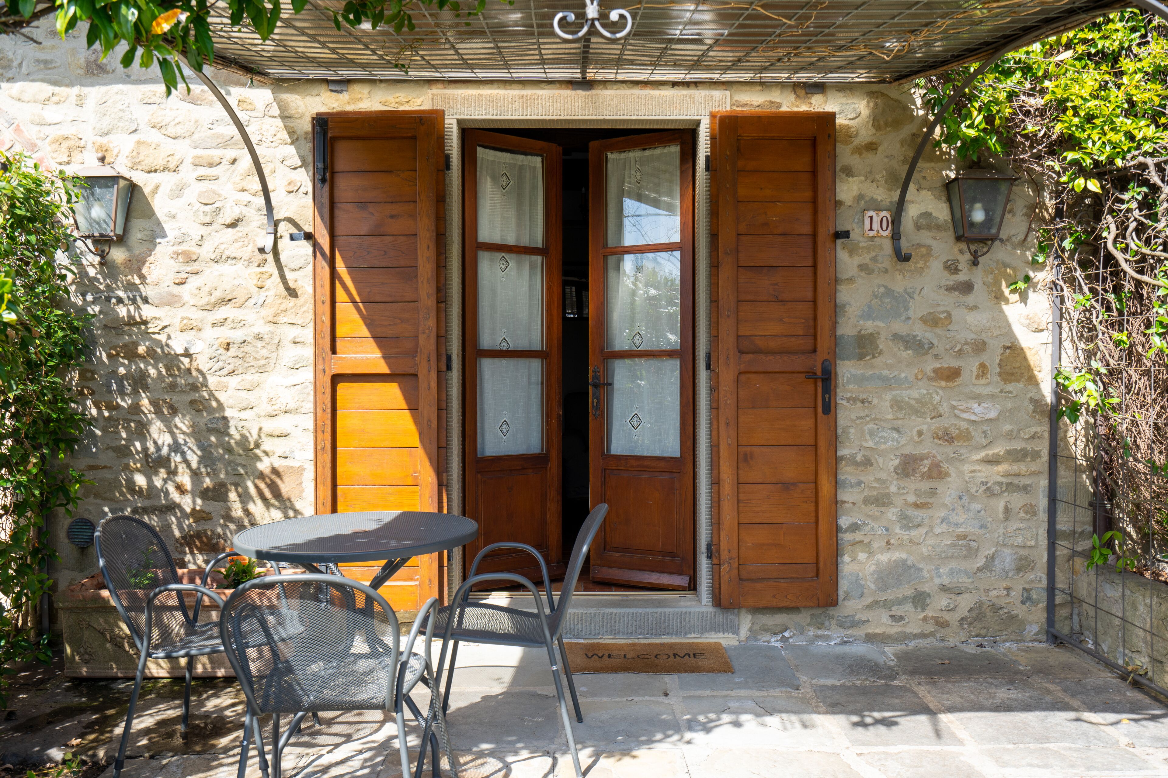 A stone building with a wooden door, a welcome mat, and a table with chairs outside.