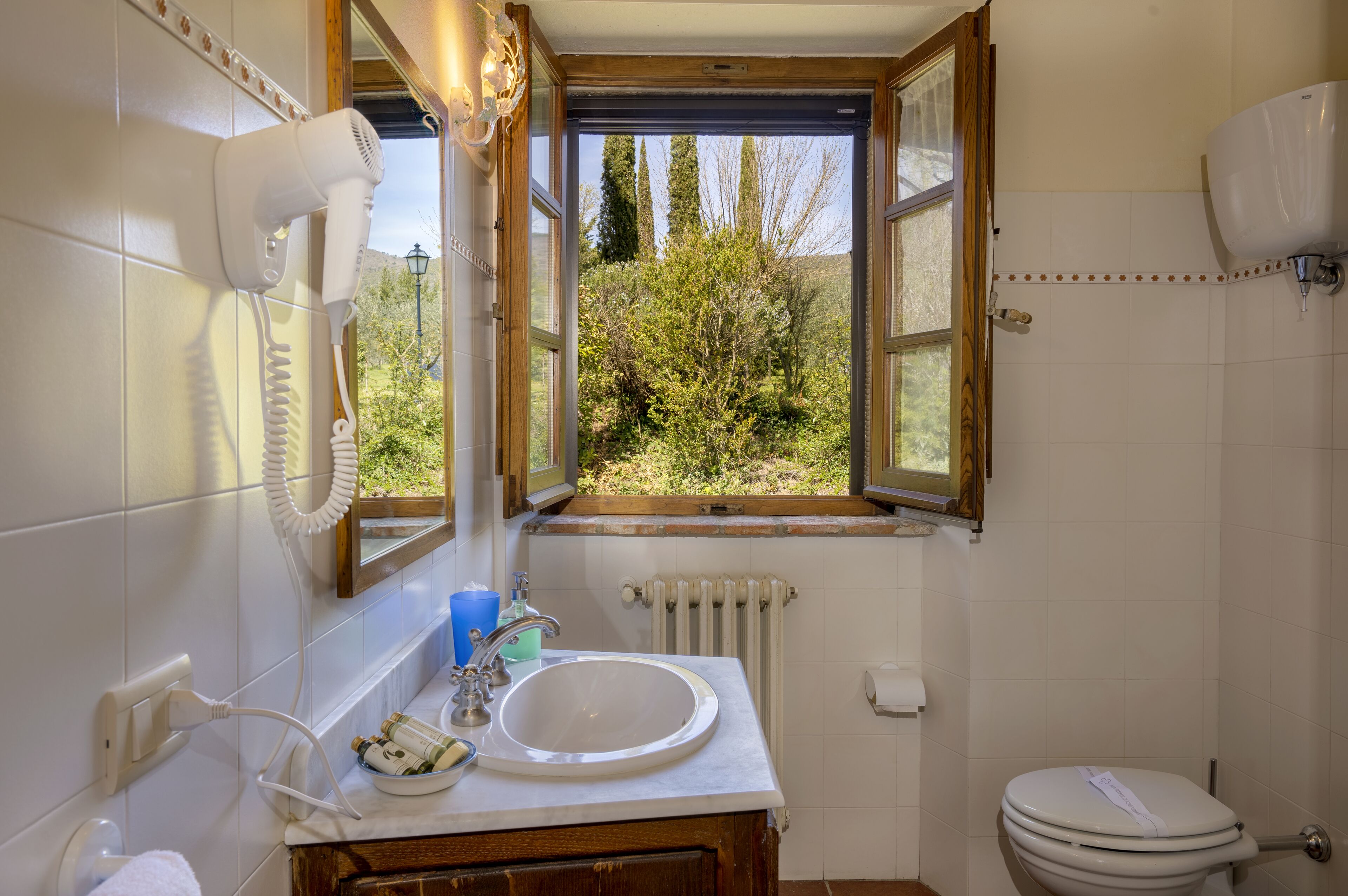 Un baño con lavamanos, inodoro y ventana con puerta abierta.