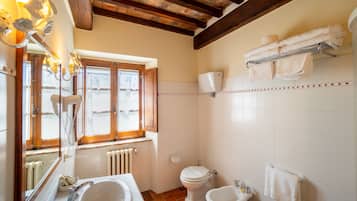 Et badeværelse med håndvask, to toiletter, et bidet, et håndklædestativ og et vindue med en radiator nedenunder.
