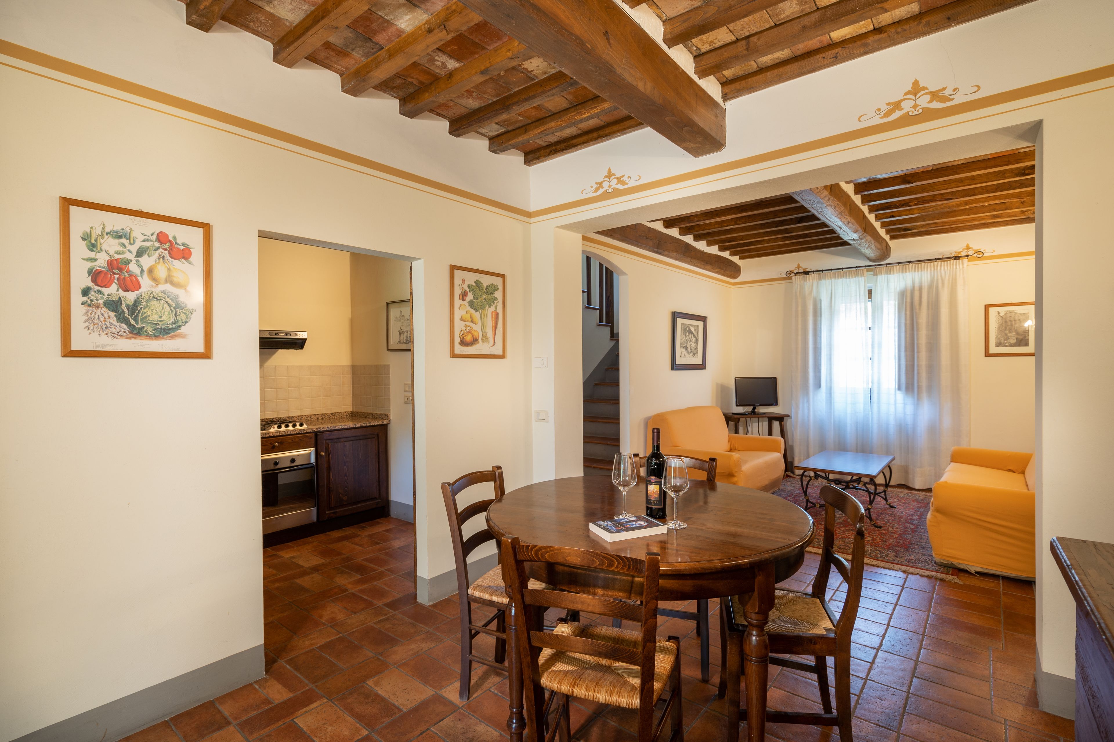 A dining area with a round table, chairs, and a book. There is a kitchen visible in the background.