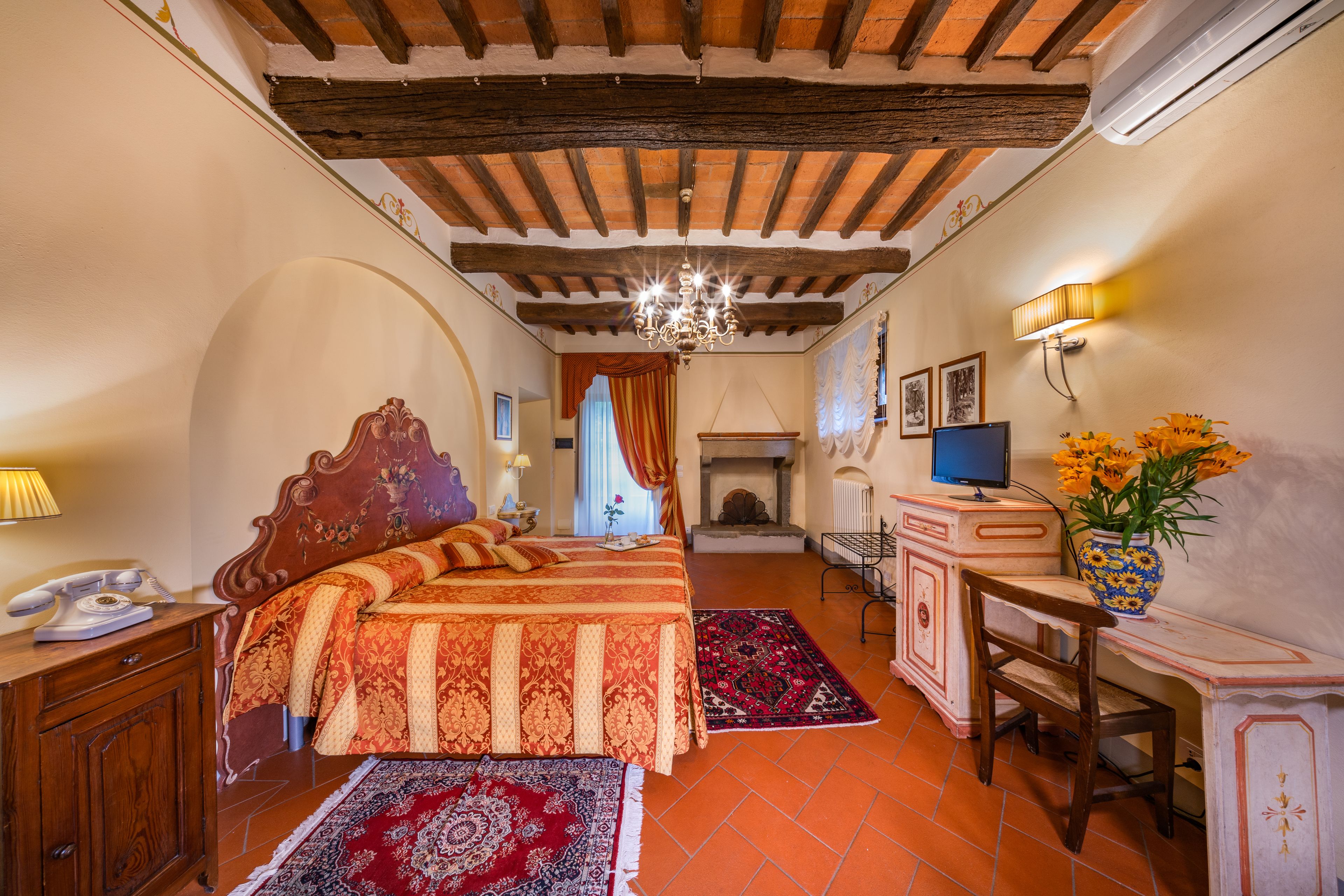 Una habitación tradicional con cama, escritorio, chimenea y candelabro.