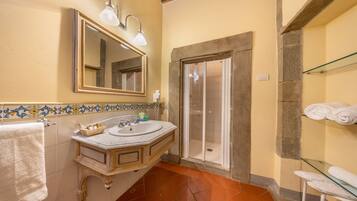 A bathroom with a marble sink, a mirror, a shower, and a glass shelf with towels.