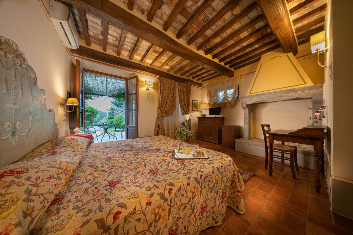 Une chambre à coucher avec une couvre-lit à motifs floraux, une table à manger avec des chaises, une cheminée et un balcon avec une table et des chaises.