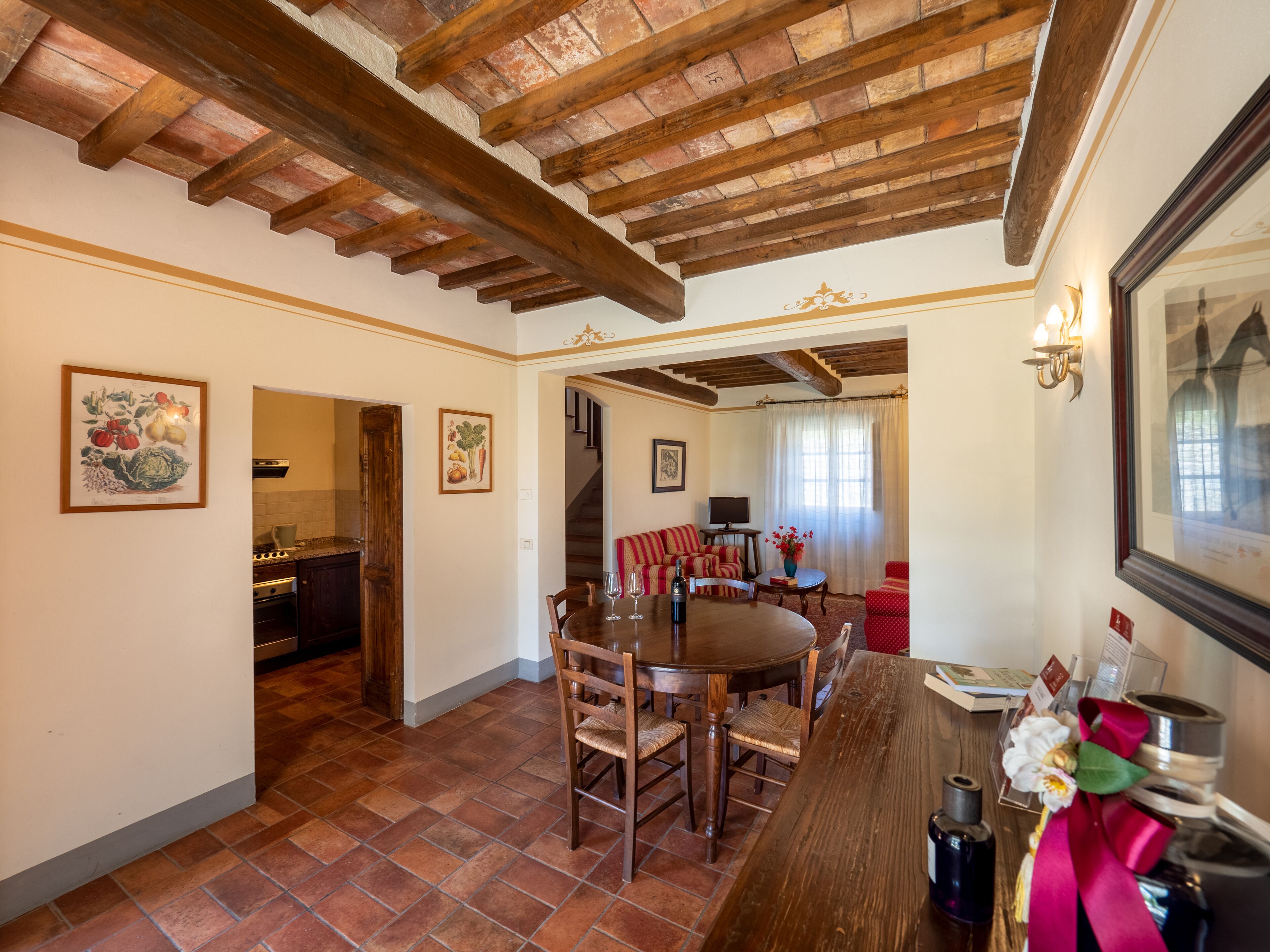 Uma área de refeições com uma mesa e cadeiras de madeira, uma cozinha ao fundo e uma escada que sobe.