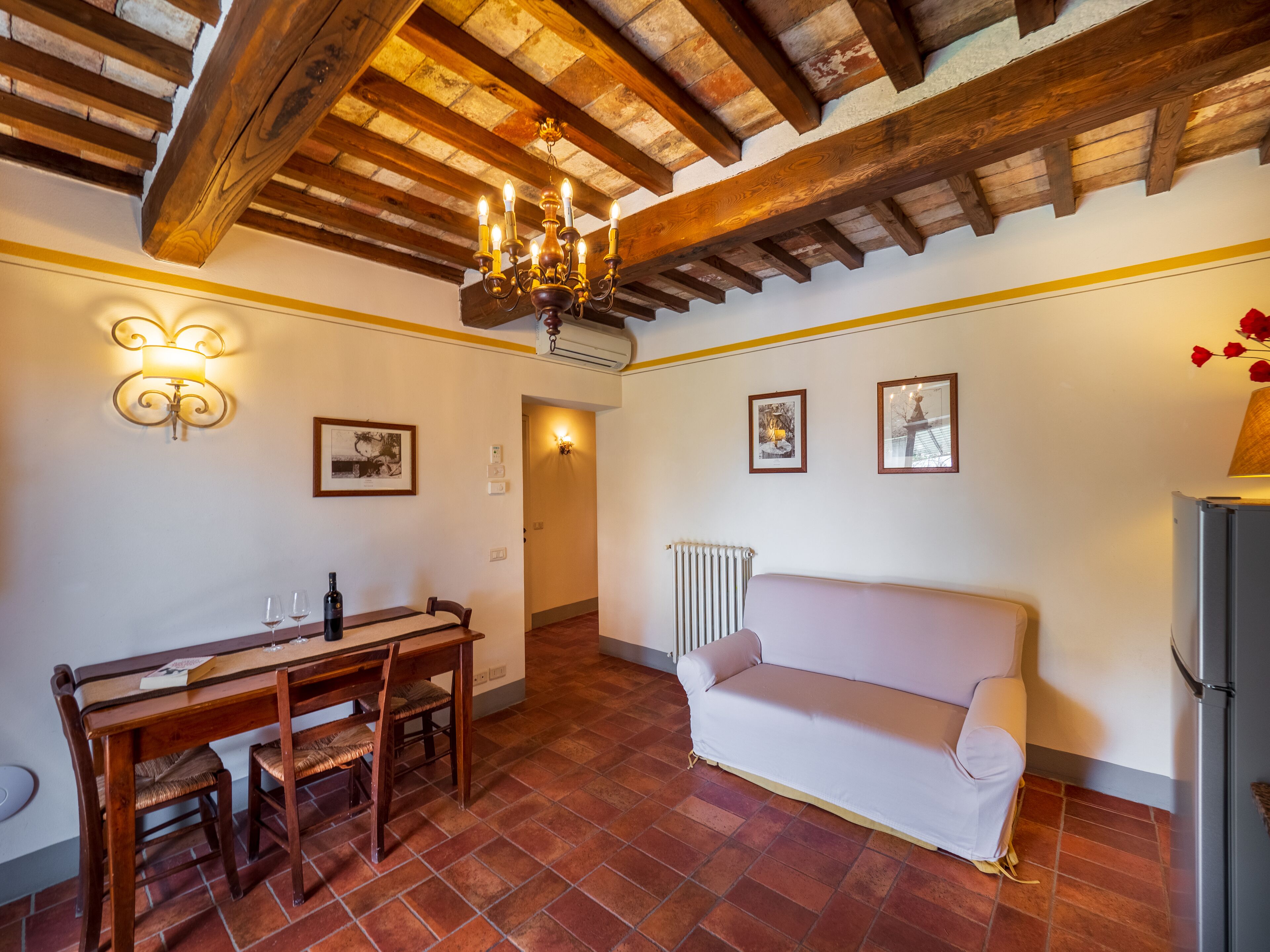 Zona pranzo con tavolo e sedie in legno, un divano bianco e un lampadario.