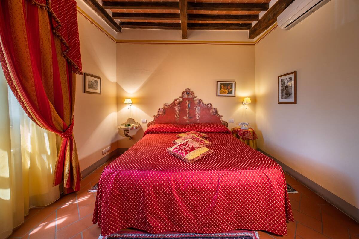 Une chambre d’hôtel avec un grand lit, des rideaux rouges et deux lampes fixées au mur.