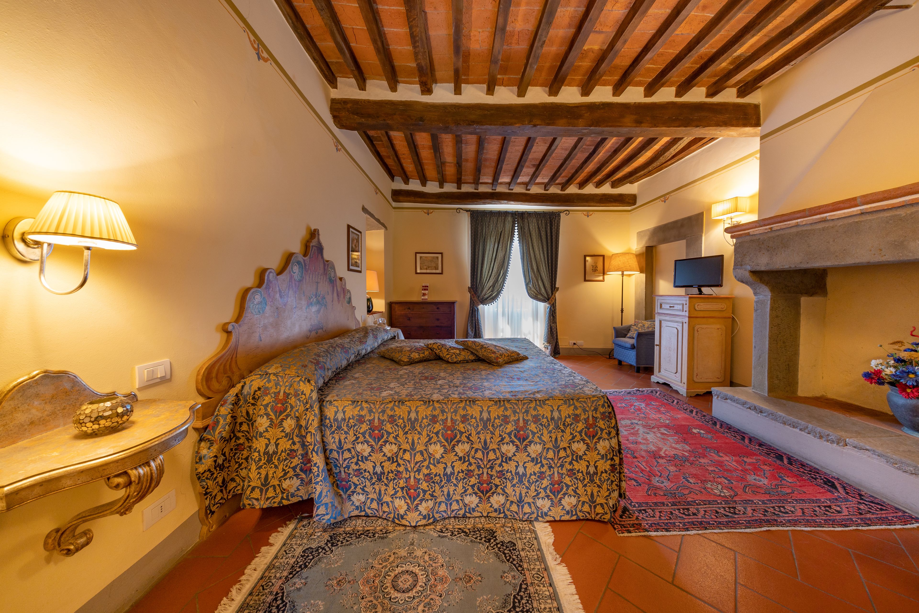 Un dormitorio con cama, mesita de noche, lámpara, televisión y chimenea.
