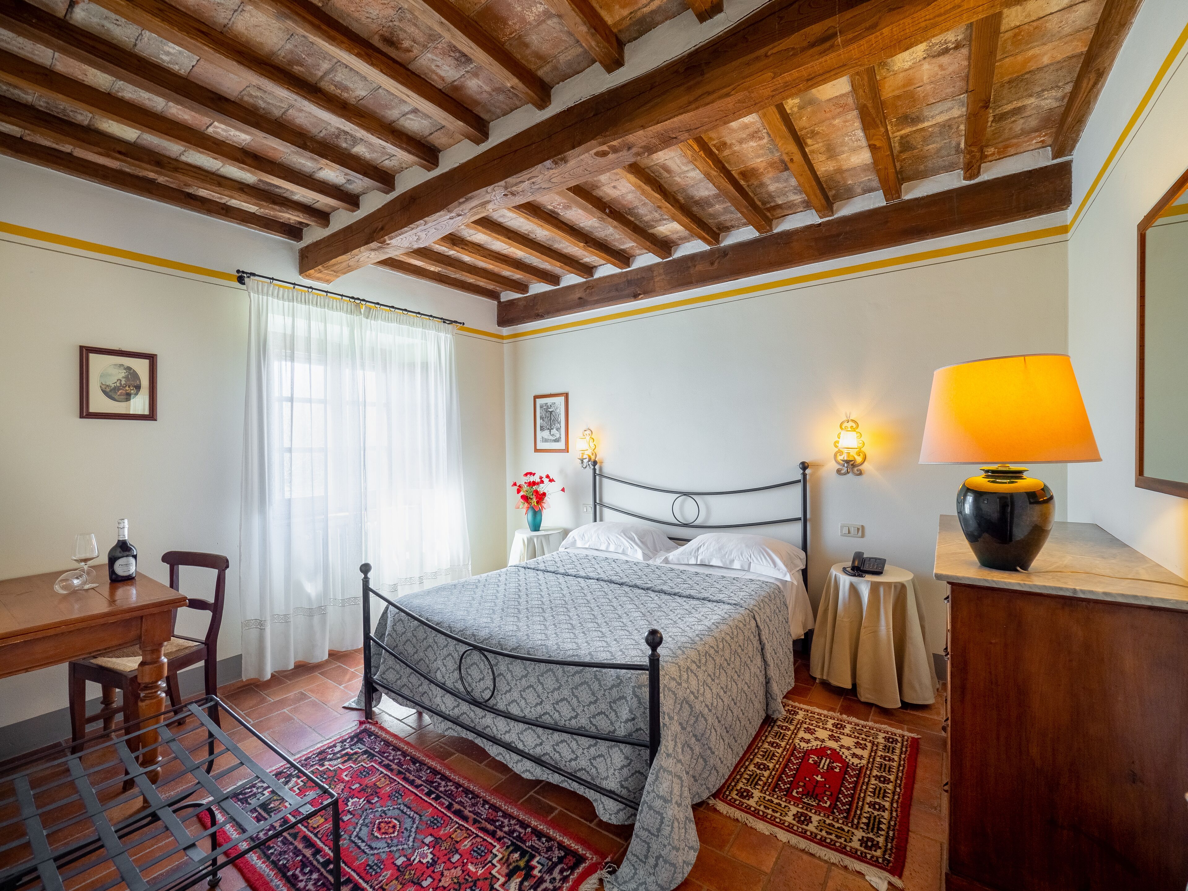 Ein Schlafzimmer mit Holzboden, einem Bett mit gemustertem Überwurf, einem Nachttisch mit Lampe, einem Sessel und einem kleinen Tisch mit Flasche und Glas.